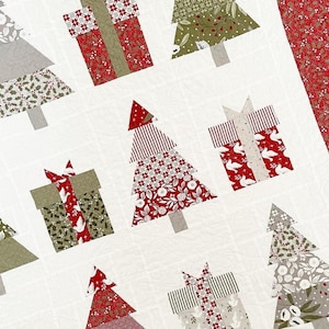 May include: A white quilt with a Christmas theme featuring red, green, and white patchwork trees and presents.