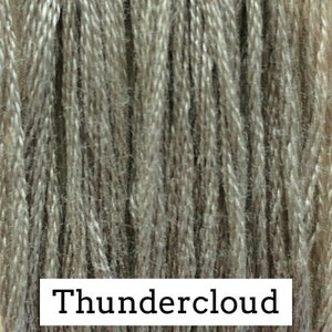 May include: Close-up of a skein of yarn in a light gray color with a subtle brown undertone. The yarn is labeled "Thundercloud".