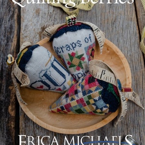 May include: Three colorful fabric pincushions shaped like strawberries in a wooden bowl. The pincushions are decorated with patchwork fabric and embroidery. The pincushions are labeled "scraps of", "quil", and "quilting berries".