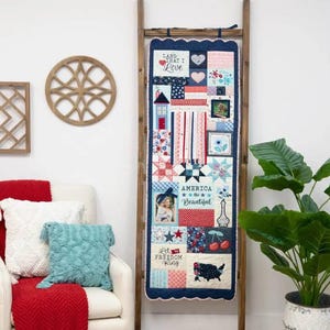 May include: A patriotic quilt with a blue, white, and red color scheme. The quilt features a variety of designs, including stars, stripes, hearts, and a picture of a woman. The quilt also includes the text "Land That I Love", "America the Beautiful", and "Let Freedom Ring".