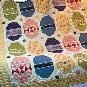 May include: A quilt with a patchwork design featuring various colors and patterns, including green, blue, pink, and yellow. The quilt is made up of octagonal shapes, each with a different design. The quilt is quilted with a decorative stitch.