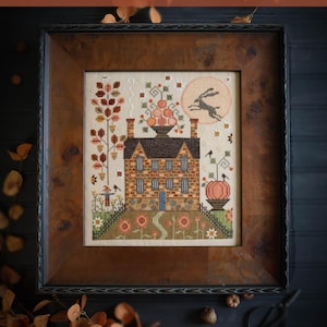 May include: Framed cross-stitch sampler titled "Autumn Moon" by Plum Street Samplers. The artwork depicts a brick house with a pumpkin, a running hare, and a full moon. The frame is dark wood.