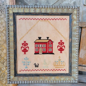 May include: A framed cross-stitch embroidery depicting a red house with a yellow roof, two trees, a swan, a crown, and two red flower pots with white flowers. The embroidery is on a beige background.