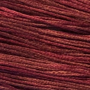 May include: Close-up of a skein of embroidery thread in shades of burgundy, brown, and tan. The threads are tightly wound, creating a textured surface. Suitable for cross-stitch, embroidery, and other needlecraft projects.