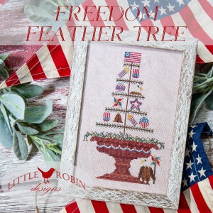 May include: A framed cross-stitch design of a red, white, and blue "Freedom Feather Tree" with an eagle holding a pinwheel. The design is by Little Robin Designs.