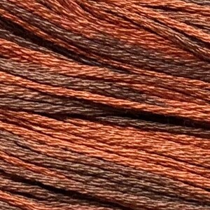 May include: Close-up of a spool of embroidery floss in a brown and orange color combination.