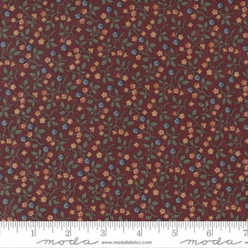 May include: A dark burgundy fabric featuring a repeating pattern of small, muted orange flowers, green leaves, and tiny blue berries on thin, winding stems. A white ruler is visible at the bottom, showing a scale of 7 inches.