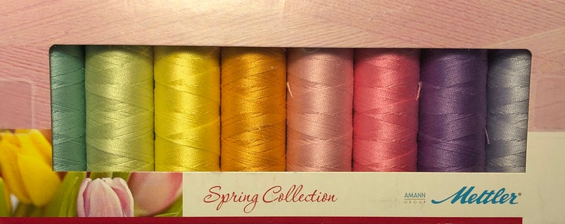 May include: A set of 10 spools of thread in pastel colors, including light green, yellow, orange, pink, and purple. The spools are labeled "Spring Collection" and "Mettler".