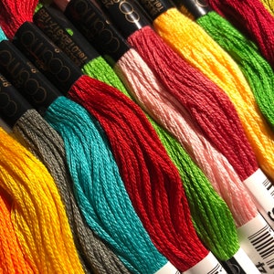 May include: A close-up of a selection of embroidery floss spools in various colours, including orange, yellow, green, red, blue, and pink. The spools are labelled with the brand name "cosmo" and a barcode.