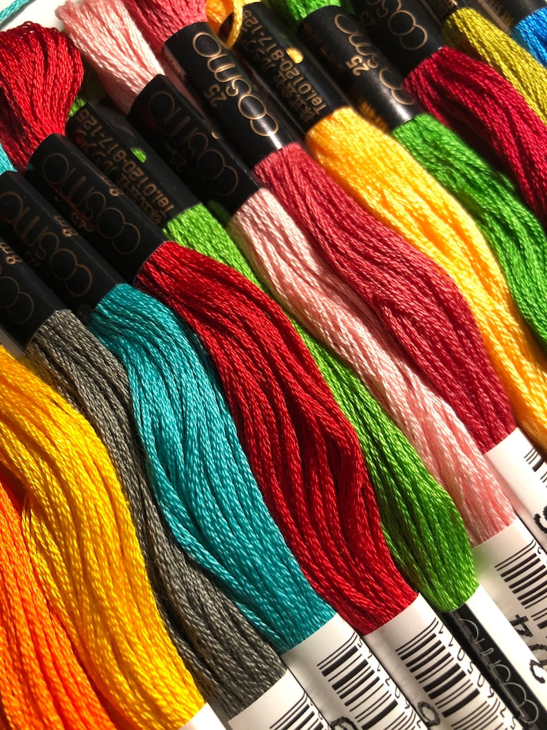 May include: A close-up of a selection of embroidery floss spools in various colours, including orange, yellow, green, red, blue, and pink. The spools are labelled with the brand name "cosmo" and a barcode.