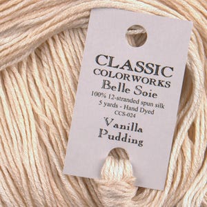 May include: A skein of off-white Belle Soie 12-stranded spun silk thread. The label reads "CLASSIC COLORWORKS Belle Soie 100% 12-stranded spun silk 5 yards - Hand Dyed CCS-024 Vanilla Pudding."