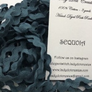 May include: A spool of teal blue rick rack trim made from 100% cotton. The trim is hand-dyed and has a wavy, scalloped edge.