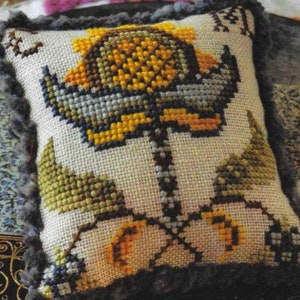 May include: A white pillow with a cross-stitch design of a yellow flower with green leaves. The pillow has a brown fringe around the edges.
