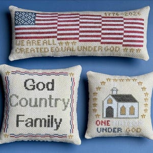 May include: Three decorative pillows with patriotic and religious themes. One pillow features an American flag design with the text "1776-2026" and "WE ARE ALL CREATED EQUAL UNDER GOD." The other two pillows have the text "God Country Family" and "ONE UNDER GOD."