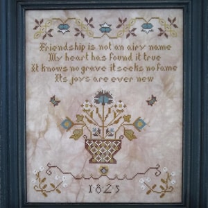 May include: Framed cross-stitch sampler with a floral basket design and the text "Friendship is not an airy name." The embroidery features blue, brown, and cream colors. The year 1825 is stitched at the bottom. The frame is dark blue.