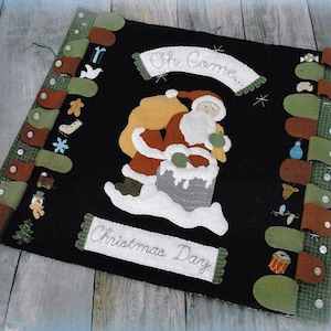 May include: A felt Christmas wall hanging with a Santa Claus figure coming down a chimney. The hanging has a banner that reads "Oh Come... Christmas Day" and is decorated with various felt ornaments.