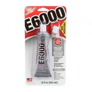 May include: A 1.0 fl oz tube of E6000 industrial strength adhesive in its original retail packaging. The gray tube features a white cap and includes precision tips. The packaging displays the product name, usage instructions, and a list of materials.