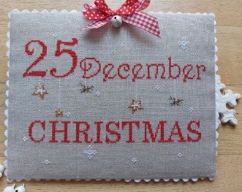 May include: A white linen cross stitch with red embroidery. The design features the text "25 December Christmas" with stars and snowflakes.