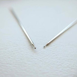 May include: Two silver knitting needles with pointed tips.