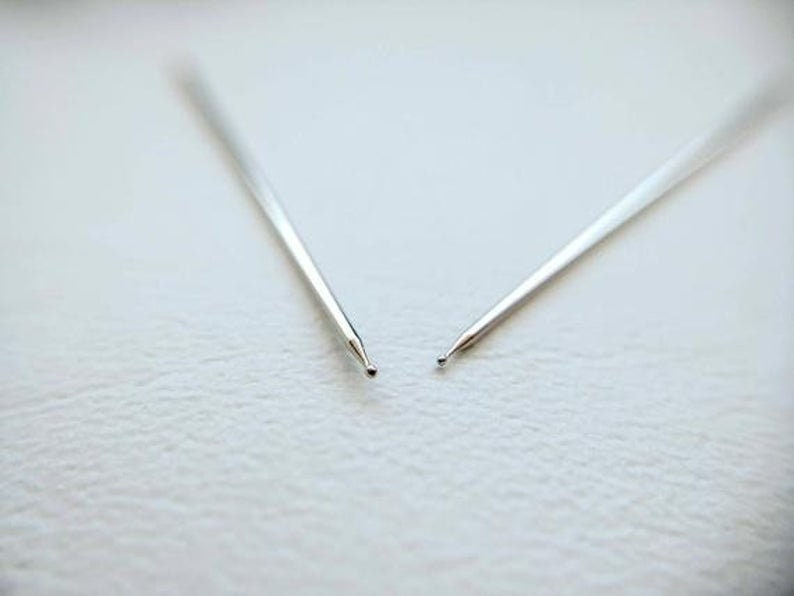 May include: Two silver knitting needles with pointed tips.