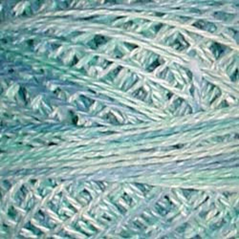 May include: Close-up of a skein of yarn in shades of blue and green. The yarn appears to be a loosely woven, open-weave style, with a mix of light and dark tones creating a textured appearance. The yarn is likely used for knitting or crochet projects.