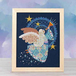 May include: Cross-stitch artwork of an angel with a trumpet, framed in light wood. The angel has patterned wings and a blue and white patterned dress. The background is dark blue with stars and a circular design.