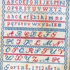 May include: A vintage cross-stitch sampler with the alphabet in red and blue thread. The sampler includes uppercase and lowercase letters, numbers, and the text "Goring x 1912 aße Io" within a decorative border.