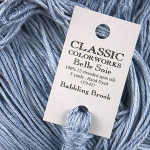 May include: A skein of light blue hand-dyed silk thread labeled "CLASSIC COLOR WORKS Belle Soie" with the color name "Babbling Brook" and the product code "CCS-027".