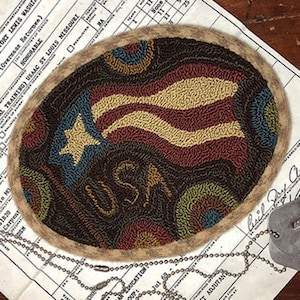 May include: A round, brown wool rug with a needlepoint design of an American flag with the word "USA" in the center. The rug is surrounded by a brown border.