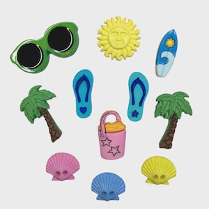 May include: A set of colourful, plastic buttons with a beach theme. The buttons feature a sun, flip flops, a palm tree, a bucket and spade, a seashell, a surfboard, and sunglasses.