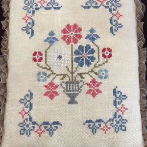 May include: A white pillow with a floral embroidery design. The flowers are in a vase and are surrounded by a border of leaves. The pillow is trimmed with a lace border.