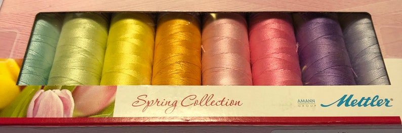 May include: A set of 10 spools of thread in pastel colors, including light green, yellow, orange, pink, and purple. The spools are labeled "Spring Collection" and "Mettler".