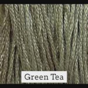 May include: Close-up of a spool of green tea-colored macrame cord. The cord is tightly wound and has a textured appearance. The text "Green Tea" is printed on a white label.