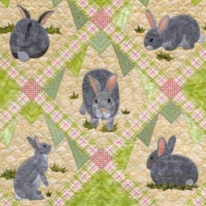 May include: A quilted textile with a repeating pattern of grey rabbits on a beige background with green and pink plaid and diamond accents. The rabbits are in different poses, creating a charming and playful design. The quilt has a handmade aesthetic.