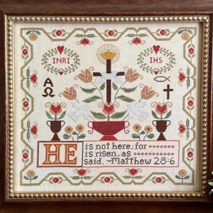 May include: Cross-stitch embroidery in a wooden frame. The design features a cross, flowers, doves, and text that reads "HE is not here; for is risen, as said. Matthew 28:6." The embroidery includes the letters INRI, IHS, and the Greek letters alpha and omega.