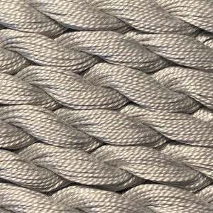 May include: Close-up of a braided silver embroidery floss. The floss is tightly woven and has a smooth, shiny finish.