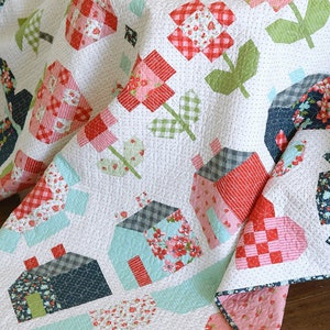 May include: A white quilt with a patchwork design featuring red, pink, green, and blue floral patterns. The quilt is folded in half and has a white background with small white dots.