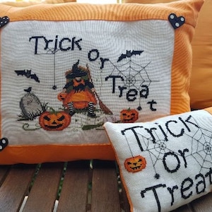 May include: Two decorative throw pillows with orange borders and black buttons. The larger pillow features an embroidered image of a witch holding a pumpkin with the text "Trick or Treat". The smaller pillow has the text "Trick or Treat" with a spider web design.