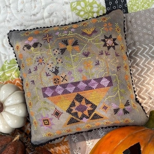 May include: A grey and orange embroidered cushion with a Halloween theme. The cushion features a black cat, pumpkins, and other autumn motifs. The cushion is decorated with a black and white trim.