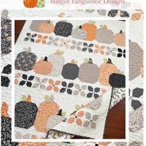 May include: A quilt with a pumpkin harvest theme. The quilt features a white background with rows of orange pumpkins, gray and beige geometric shapes, and black and white floral designs. The quilt is folded in half and the text "Pumpkin Harvest" is displayed below the quilt.