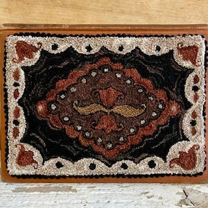 May include: A brown, black, and white rug with a geometric design. The rug has a central motif of a stylized mustache.
