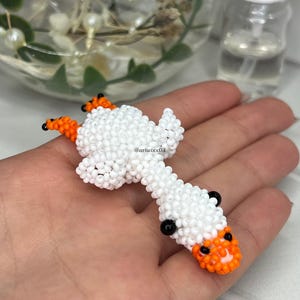 Pu&ograve; includere: Una piccola statuetta di perline fatta a mano a forma di oca, realizzata con minuscole perline bianche per il corpo e la testa, con perline arancioni vivaci per le zampe e il becco. L'oca presenta due piccole perline nere per gli occhi e il testo @ariwixx08.