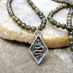 Peut inclure: Un collier de pierres précieuses vertes avec un pendentif en argent représentant un serpent doré. Le pendentif est en forme de diamant.
