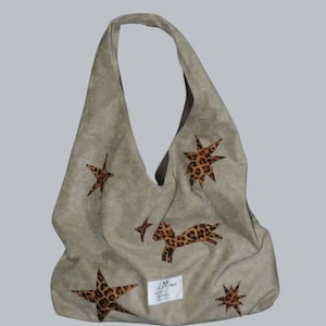 Puede incluir: Bolso hobo de ante beige con una sola correa para el hombro. El bolso está decorado con estrellas con estampado de leopardo y un leopardo saltando. Una pequeña etiqueta blanca con un logotipo está cosida en la parte delantera.