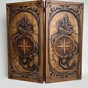 May include: Two wooden panels with nautical carvings. Each panel features a detailed relief of a sailing ship, compass rose, anchor, and rope detailing. The panels are hinged together and have a dark brown finish.
