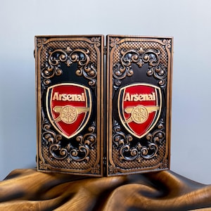 May include: A wooden box with intricate carvings and a red and gold Arsenal Football Club logo on each side.