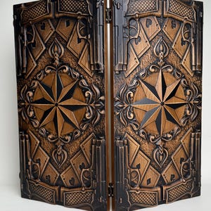 May include: A two-panel wooden screen with a detailed, carved design. The screen features a compass rose, playing card suits, and ornate scrollwork in shades of brown and black. The panels are connected by hinges.
