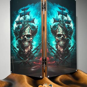 May include: A wooden game board with two glass panels featuring a skull and a pirate ship in a blue and black color scheme. The panels are hinged together and the board is sitting on a wooden surface with game pieces scattered around it.