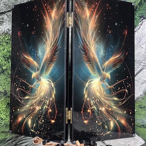May include: A folding backgammon board featuring a black surface with a vibrant, glowing phoenix illustration in shades of orange, yellow, and blue. The set includes a collection of circular wooden and black game pieces along with three blue dice.