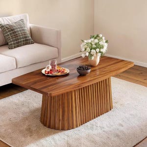 May include: A wooden coffee table with a dark brown, rectangular top and a ribbed base. The table is placed on a light-coloured rug. A vase of white flowers sits on the table. The table's dimensions are approximately 150 cm long and 75 cm wide.